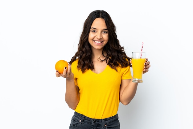 Młoda kobieta na białym tle trzyma pomarańczę i sok pomarańczowy