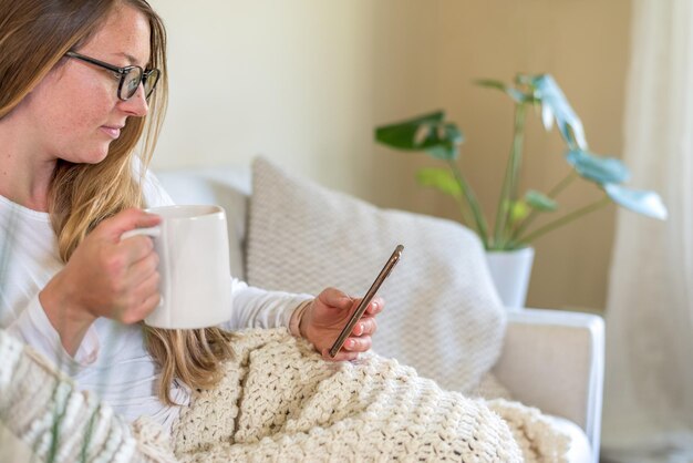 Zdjęcie młoda kobieta na kanapie z filiżanką kawy i smartfonem.