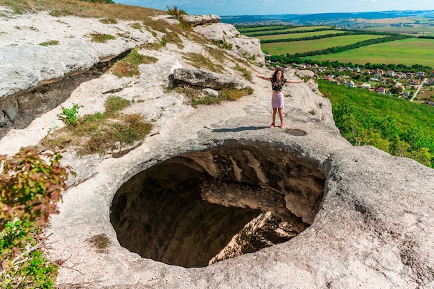 Młoda kobieta na skraju przepaści w postaci ogromnej dziury w ziemi wśród zielonych pól