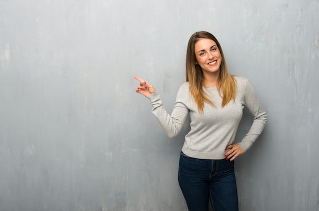 Młoda kobieta na teksturowanej ścianie wskazując palcem na bok i prezentacji produktu