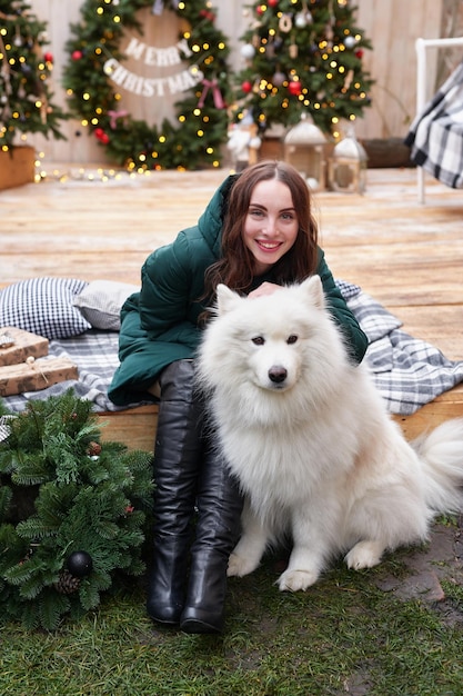 Młoda kobieta na tle choinki z białym samoyed psem na zewnątrz Dekoracja podwórka na Nowy Rok