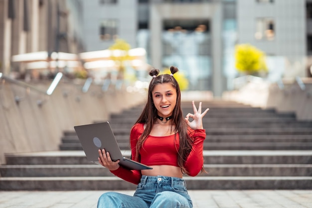 Młoda kobieta na ulicy za pomocą laptopa i pokazuje ok