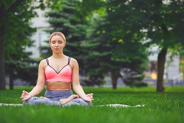 Młoda kobieta na zewnątrz, ćwiczenia medytacyjne. Dziewczyna robi lotos dla relaksu. Wellness, spokój, relaks, zdrowy, aktywny styl życia