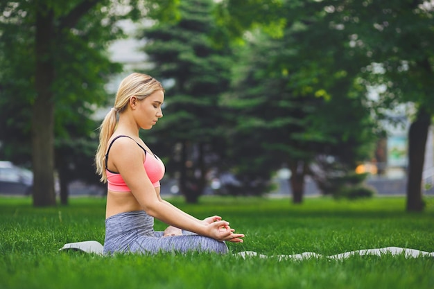 Młoda kobieta na zewnątrz, ćwiczenia medytacyjne. Dziewczyna robi lotosu dla relaksu, widok z boku. Wellness, spokój, relaks, zdrowy, aktywny styl życia