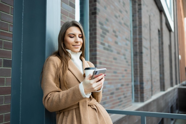 Młoda kobieta na zewnątrz z filiżanką kawy za pomocą smartfona