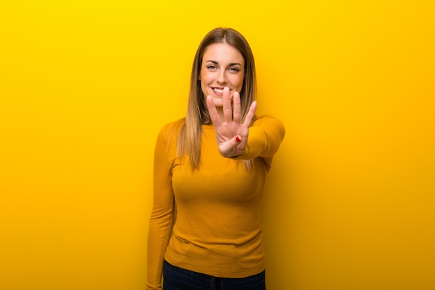 Młoda kobieta na żółtym tle szczęśliwym i liczenie cztery z palcami
