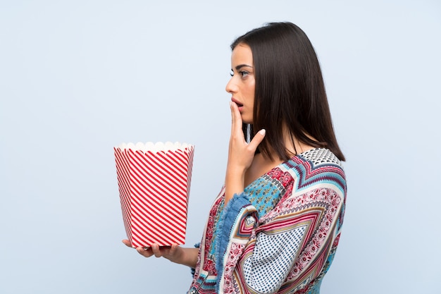 Młoda kobieta nad odosobnioną błękit ścianą trzyma puchar popcorns