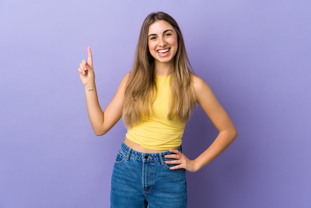 Młoda kobieta nad odosobnioną fioletową ścianą pokazując i podnosząc palec na znak najlepszych