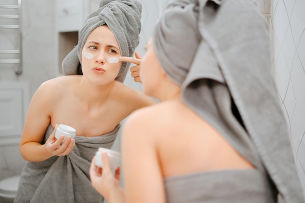 Zdjęcie młoda kobieta nakłada krem na policzki, aby zwalczyć starzenie się skóry twarzy. pojęcie kosmetologii.