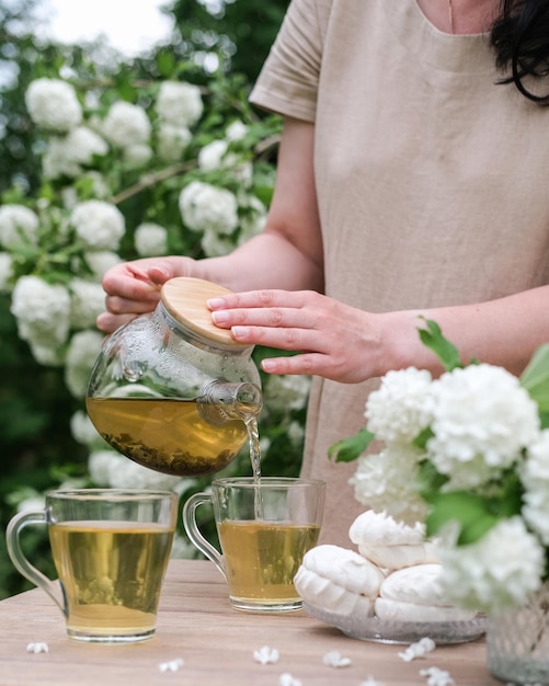 Zdjęcie młoda kobieta nalewa herbatę z czajnika do filiżanki na tle kwitnącego ogrodu