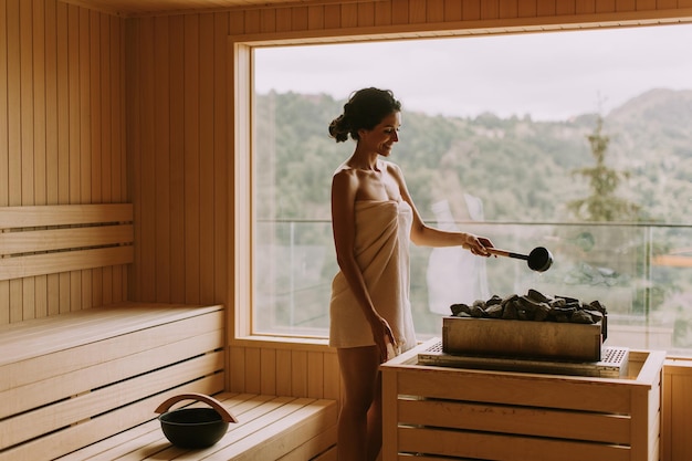 Młoda kobieta nalewa wodę na gorący kamień w saunie