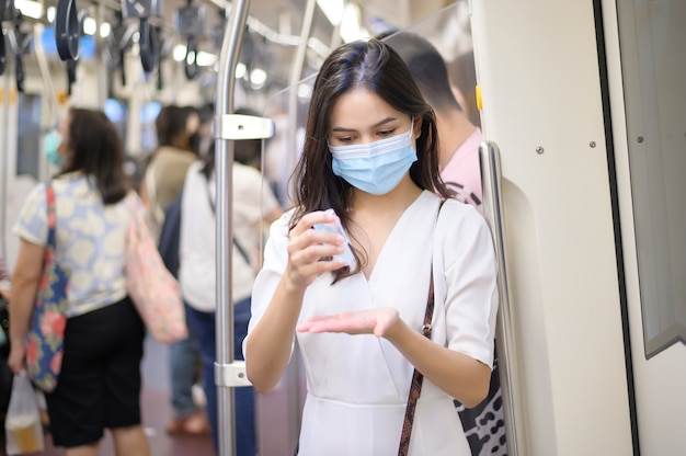 Młoda kobieta nosząca maskę ochronną w metrze używa alkoholu do mycia rąk, podróżuje w czasie pandemii Covid-19, podróżowania w celach bezpieczeństwa, protokołu dystansu społecznego