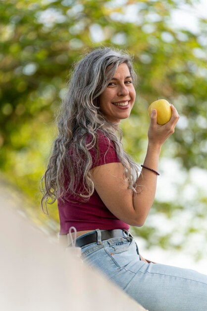 Młoda kobieta o siwych włosach zjada jabłko na zewnątrz