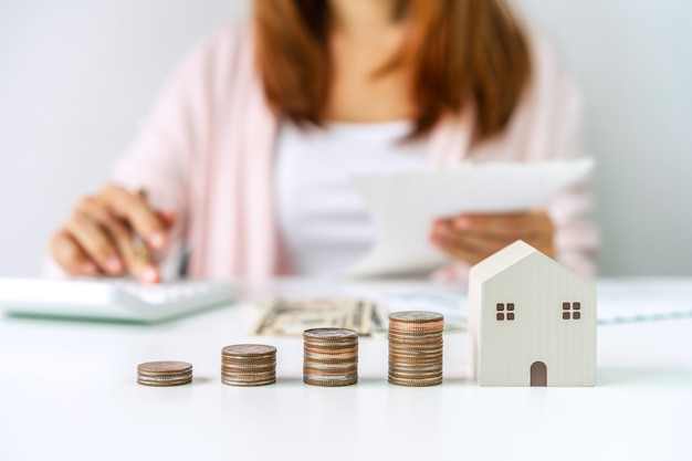 Zdjęcie młoda kobieta obliczania wydatków domowych ze stosem monet, oszczędzając pieniądze na koncepcję inwestycji w nieruchomości