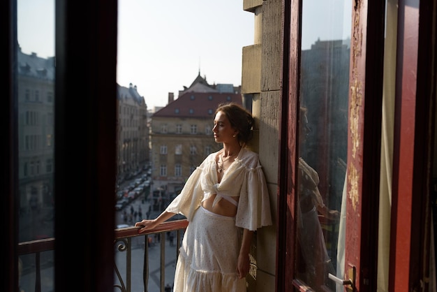 Młoda kobieta odpoczywa na balkonie swojego mieszkania z widokiem na stare miasto