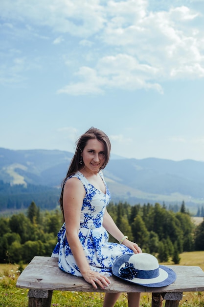 Młoda kobieta odpoczywa na ławce w górach w eleganckiej sukni