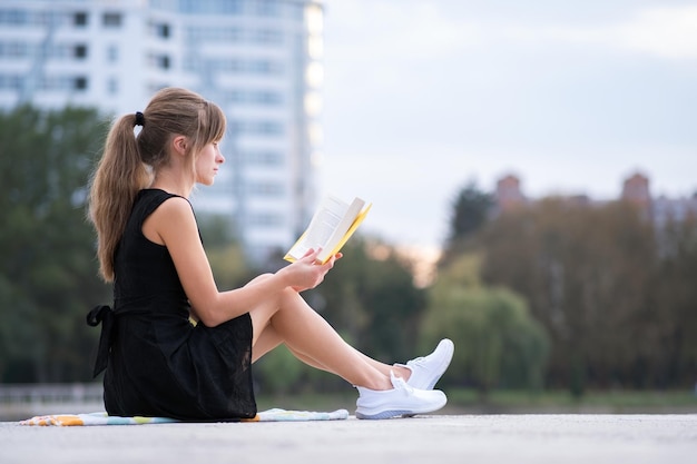 Młoda kobieta odpoczywa w letnim parku, czytając książkę Koncepcja edukacji i sudy