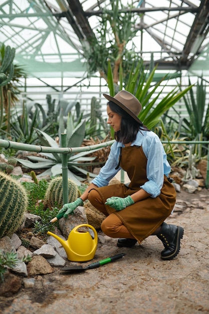 Młoda kobieta ogrodniczka z narzędziami ogrodniczymi opiekująca się kaktusami pracującymi w szklarni. Proces sadzenia sadzonek