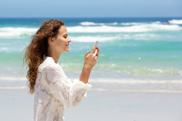 Młoda kobieta ono uśmiecha się z telefonem komórkowym przy plażą