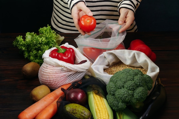 Młoda kobieta pakowania świeżych organicznych warzyw w torby ekologiczne na drewnianym stole.