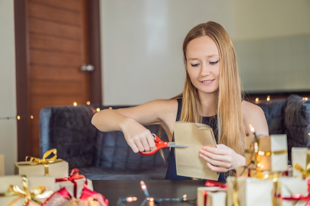 Zdjęcie młoda kobieta pakuje prezenty. prezent zawinięty w papier rzemieślniczy z czerwono-złotą wstążką na boże narodzenie