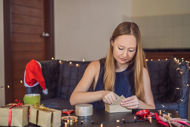 Młoda kobieta pakuje prezenty zapakowane w papier rzemieślniczy z czerwono-złotą wstążką dla