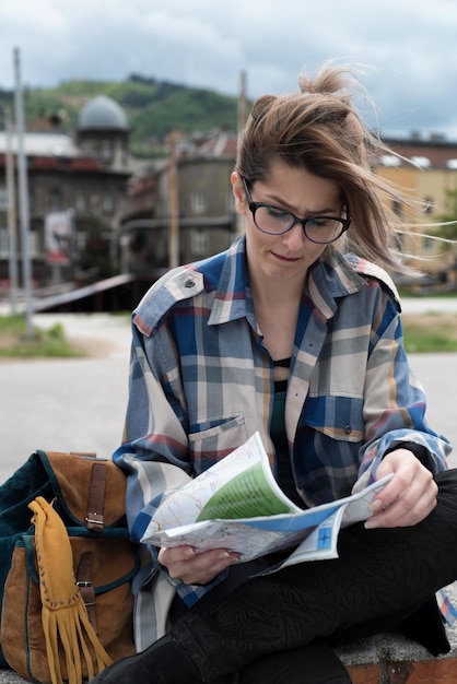 Zdjęcie młoda kobieta patrząca na mapę siedząc przy budynkach