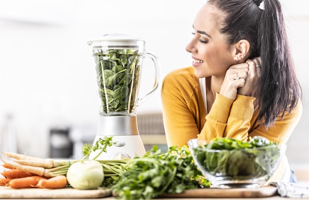 Zdjęcie młoda kobieta patrzy na otaczający ją blender pełen świeżych warzyw ze szpinakiem