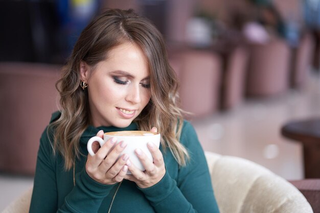 Zdjęcie młoda kobieta pije cappuccino w kawiarni.