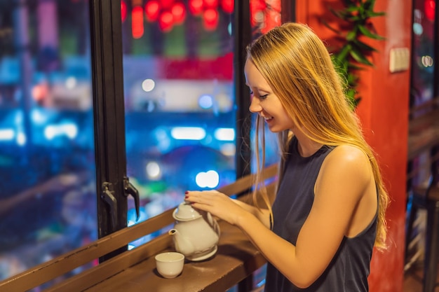 Młoda kobieta pije chińską herbatę na tle czerwonych chińskich lampionów na cześć chińskiej nowości