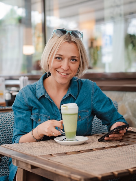 Młoda kobieta pije cieszący się matcha zielonej herbaty latte w lato ranku w kawiarni.
