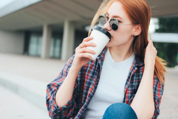 Zdjęcie młoda kobieta pije kawę w filiżance, siedząc na zewnątrz