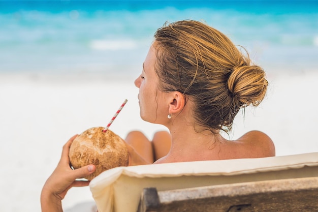 Młoda kobieta pije mleko kokosowe na bryczce na plaży. Dream scape Ucieczka z piękną dziewczyną. Korzyści z wody kokosowej.