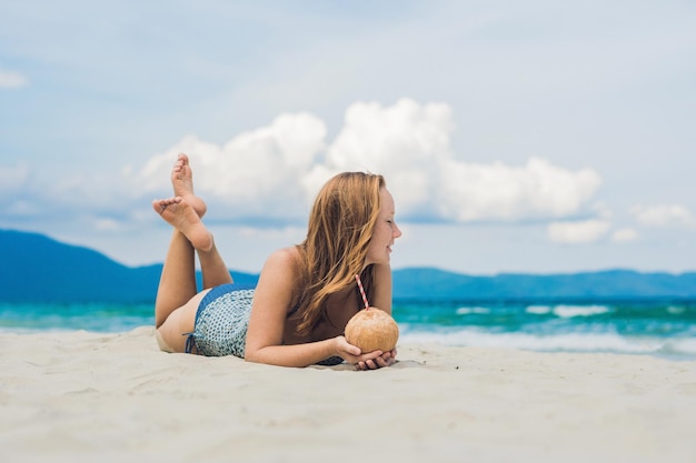 Młoda kobieta pije mleko kokosowe na plaży. Dream scape Ucieczka z piękną dziewczyną. Korzyści z wody kokosowej.