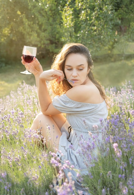 Młoda kobieta pije wino na polu lawendy o zachodzie słońca