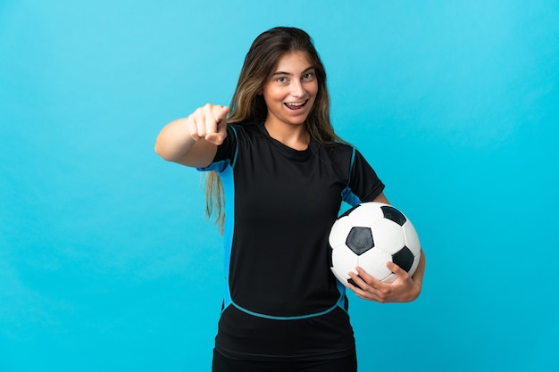 Młoda kobieta piłkarz na białym tle na niebieskiej ścianie zaskoczony i wskazując przód