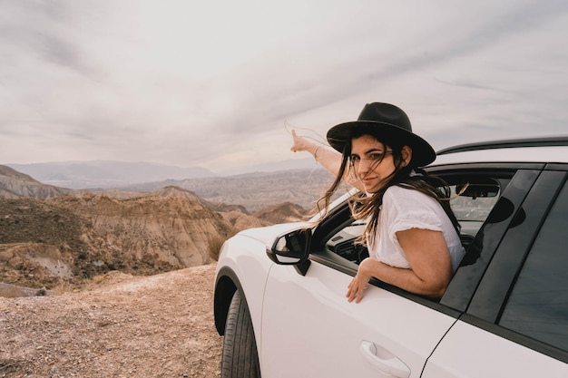 Młoda kobieta podziwia pustynny krajobraz z samochodu o zachodzie słońca