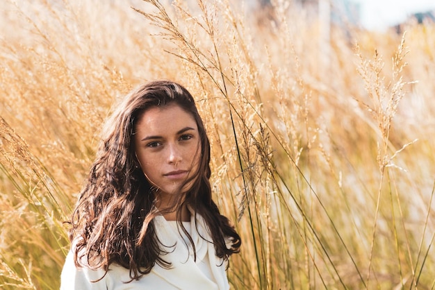Młoda kobieta pozuje do portretu przed krzakiem gęstej trawy. Bardzo ładna pozuje dziewczyna z milenialsów