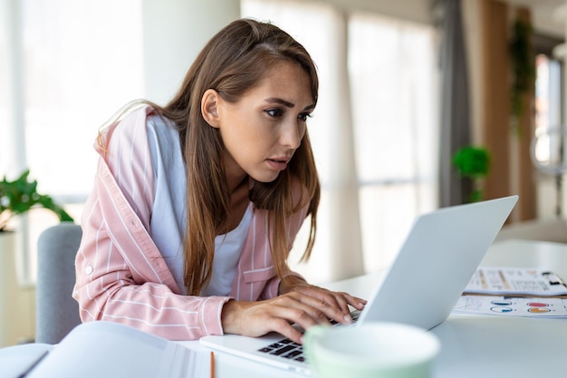 Młoda kobieta pracująca na laptopie Biznesowa kobieta zajęta pracą na laptopie w biurze Kobieta siedzi przy jasnym, nowoczesnym stanowisku pracy i pisze na laptopie