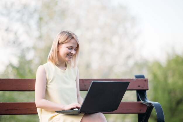 młoda kobieta pracująca zdalnie w letnim parku z samoizolacją laptopa