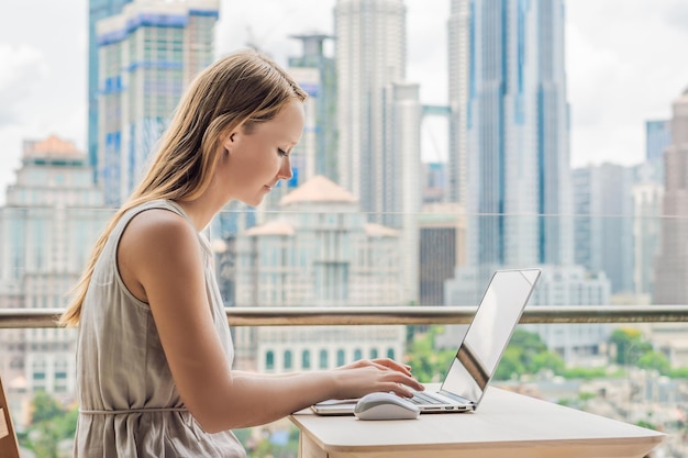 Młoda kobieta pracuje na laptopie na swoim balkonie z widokiem na drapacze chmur freelancer, praca zdalna