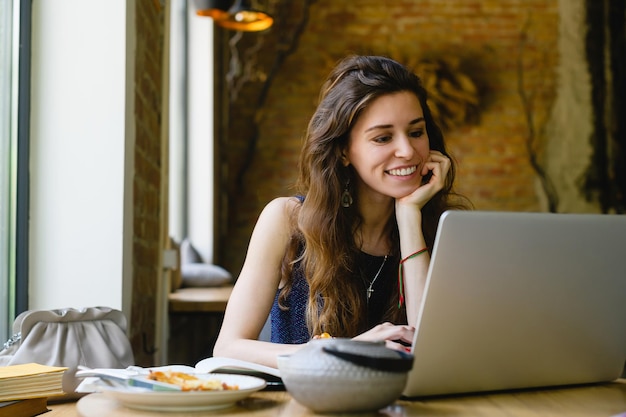 Młoda kobieta pracuje na laptopie siedząc w kawiarni