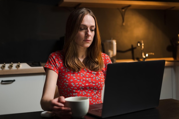 Młoda kobieta pracuje na laptopie w kuchni Praca na zlecenie w nocy w domu Nieregularny harmonogram pracy