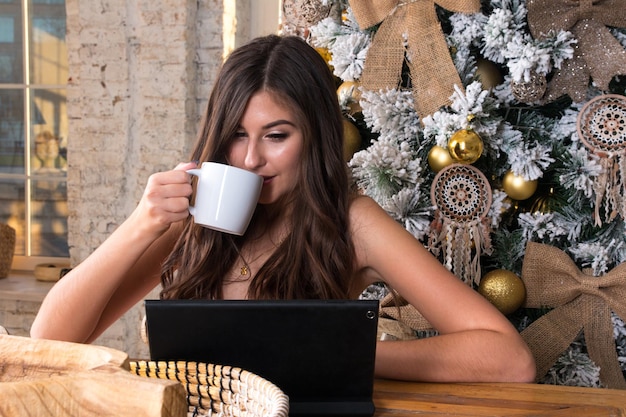 Młoda kobieta pracuje przy komputerze przy filiżance kawy. Poddaj kwarantannie samoizolację na odległej choince za plecami