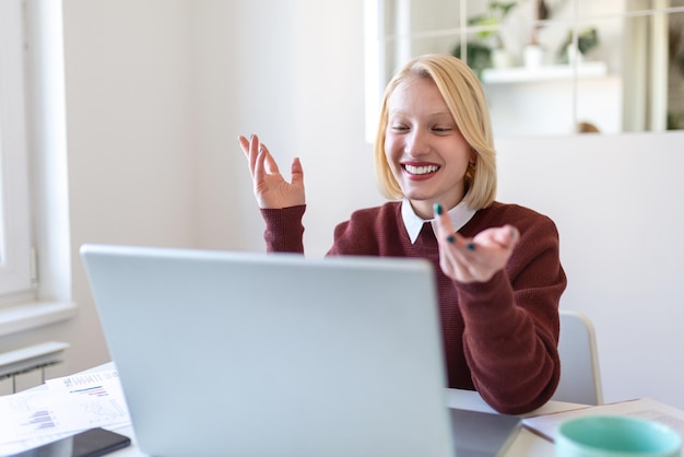 Młoda kobieta pracuje zdalnie na laptopie w swoim mieszkaniu. Pani podczas spotkania biznesowego wideo w domu. Ładna studentka słuchająca wykładu online.