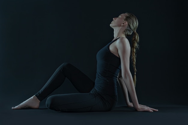 Młoda kobieta praktykuje pozycję jogi. Mata do jogi i legginsy na ciemnym czarnym tle. skopiuj miejsce.