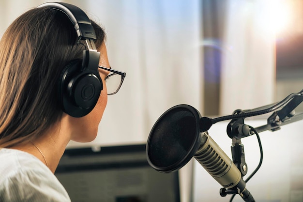 Młoda kobieta prowadząca talk show ze swojego studia w słuchawkach rozmawiająca z mikrofonem