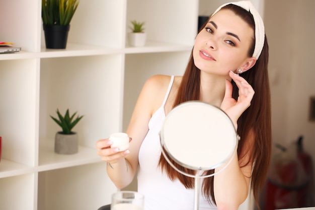 Młoda kobieta przed lustrem stosowania produktów do pielęgnacji twarzy