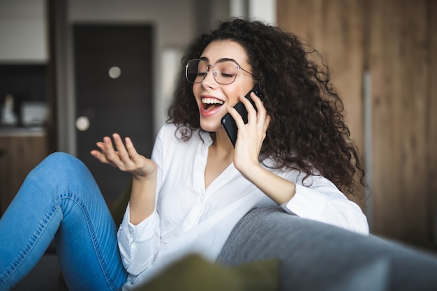 Młoda kobieta przy użyciu telefonu komórkowego, siedząc na kanapie w domu