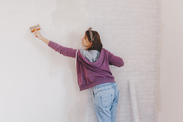 Zdjęcie młoda kobieta przykleja tapetę w domu. dziewczyna klei tapetę w formie cegły. naprawic.